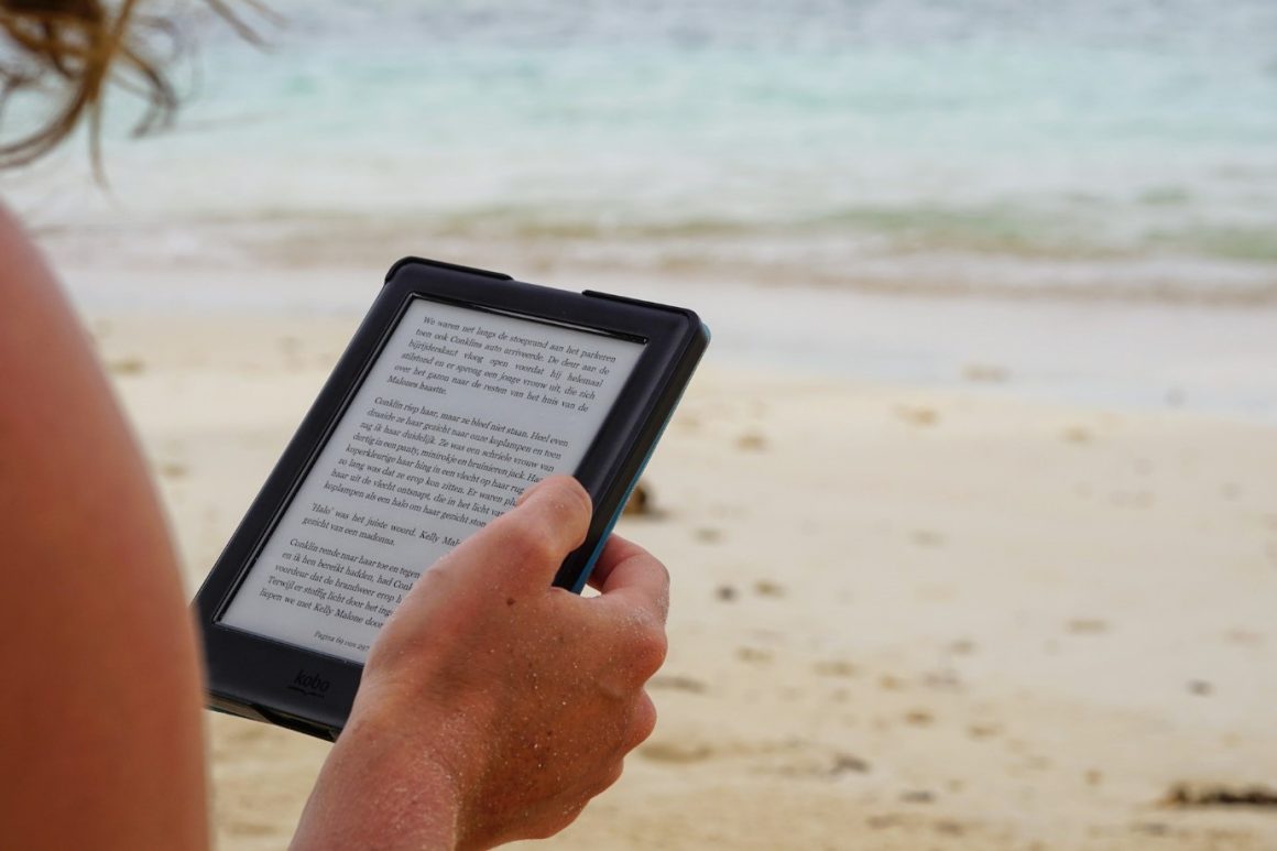 Reading a book on an e-reader at the beach.