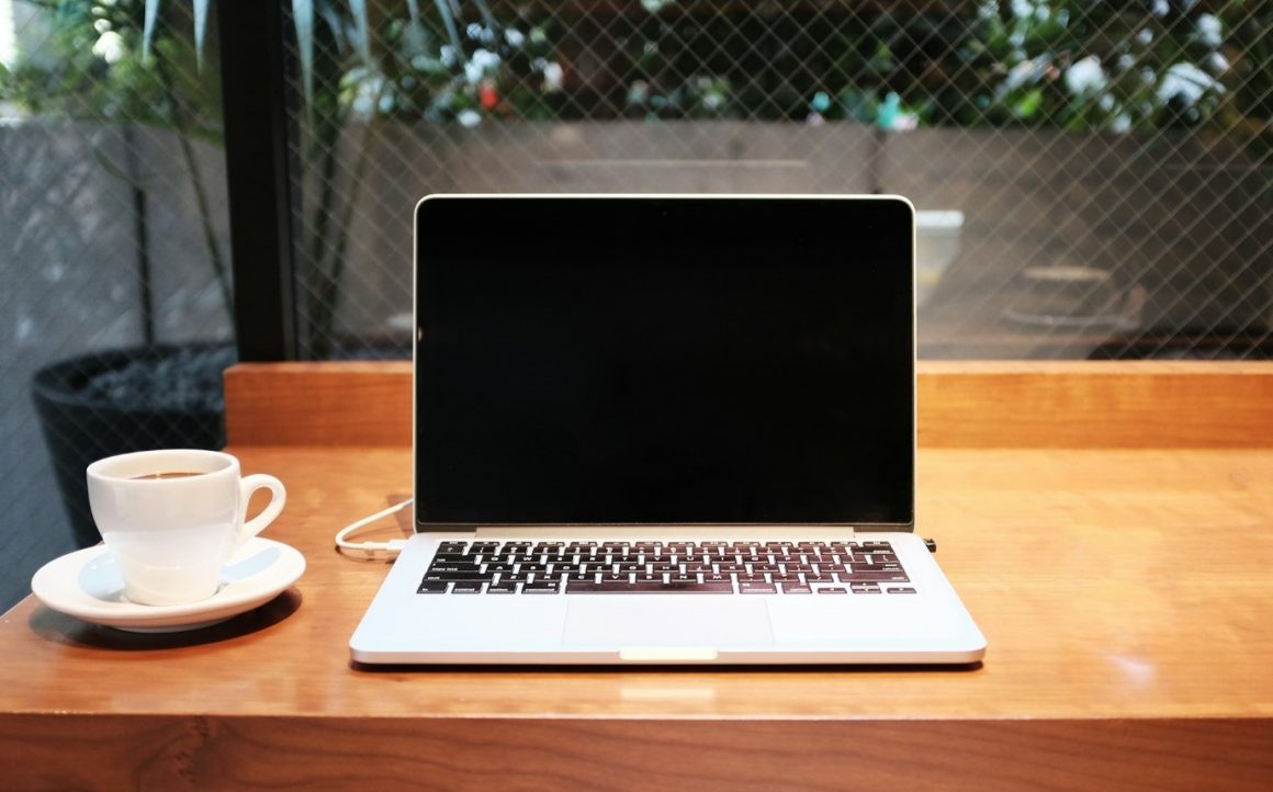 A laptop and coffee cup on a wooden table.  