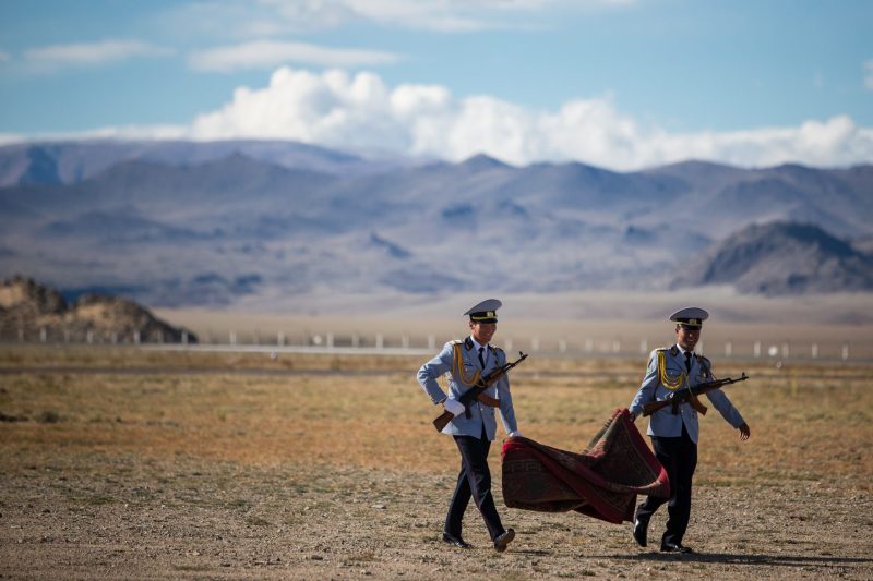 Soldiers carrying a ceremonial red carpet across the Mongolian steppe for an official arrival.