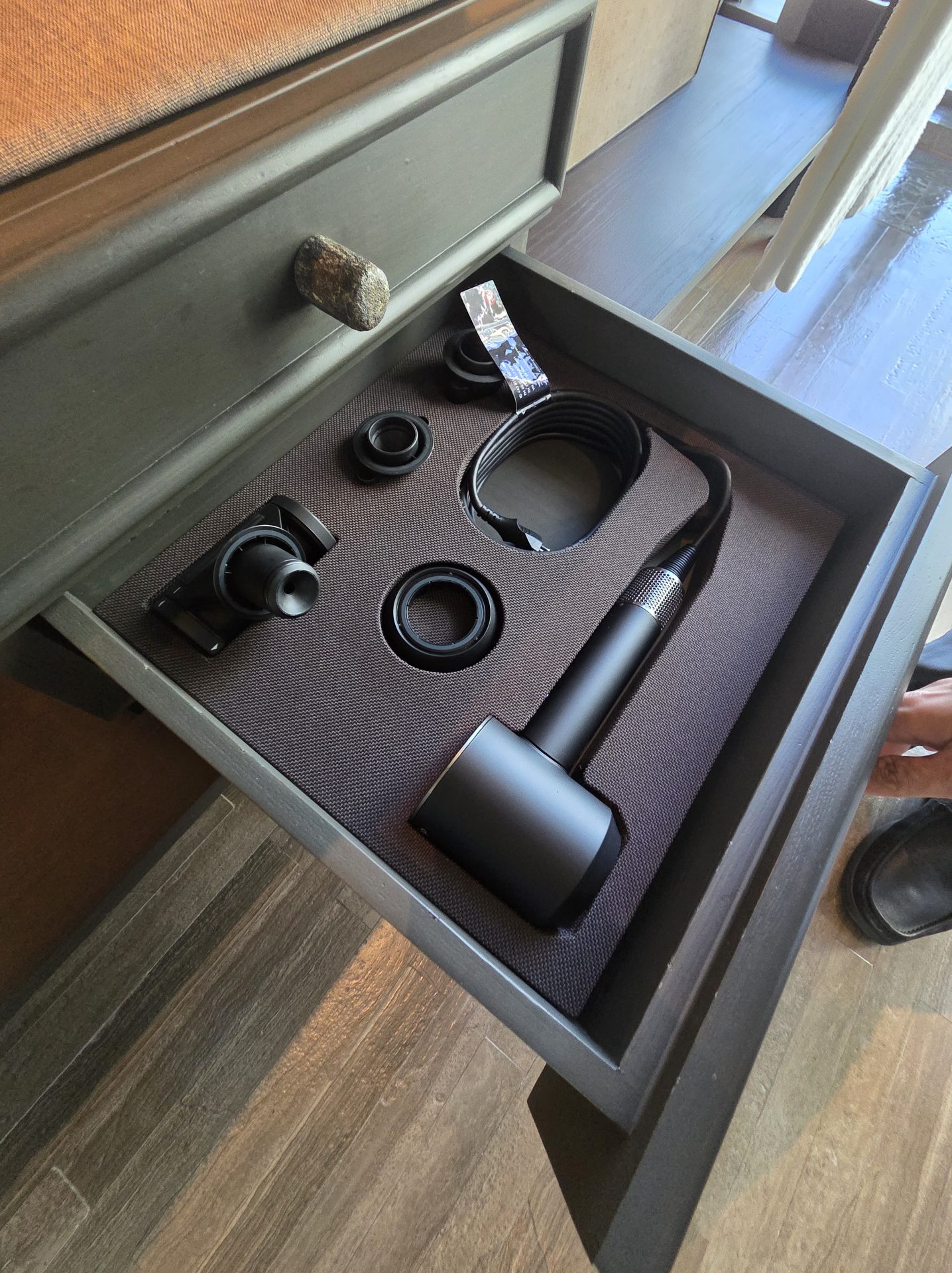 Open vanity drawer at Aman Nai Lert Bangkok revealing a Dyson Airwrap hair styling tool with all its attachments neatly arranged in a fitted fabric tray