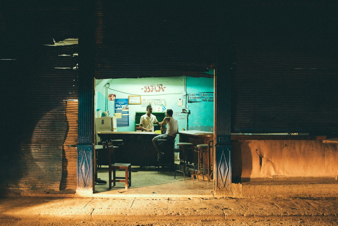 Two men talk inside a small neighborhood bar at night in Havana, Cuba. Photo by Hélène Havard.