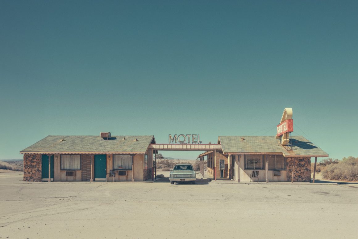 Vintage roadside motel in a desert landscape with a classic car parked outside. Photo by Hélène Havard.