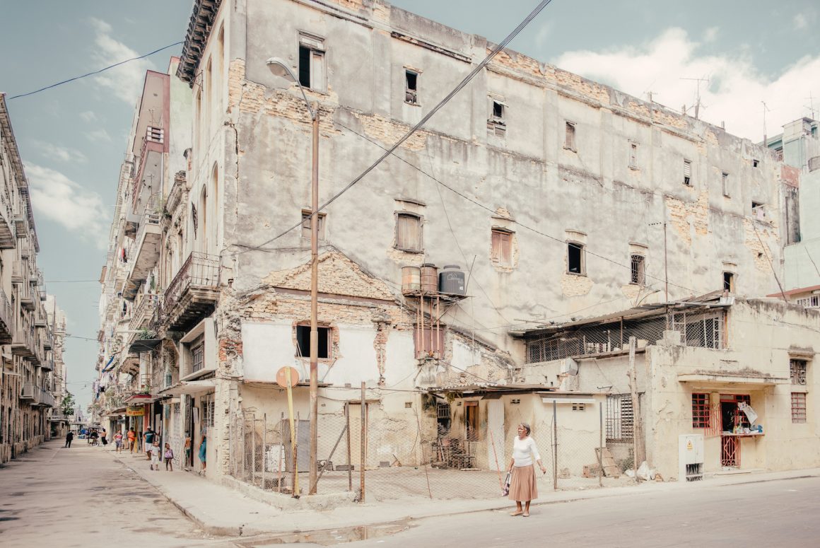 A woman stands beside a weathered building on a residential street in Havana, Cuba. Photo by Hélène Havard.