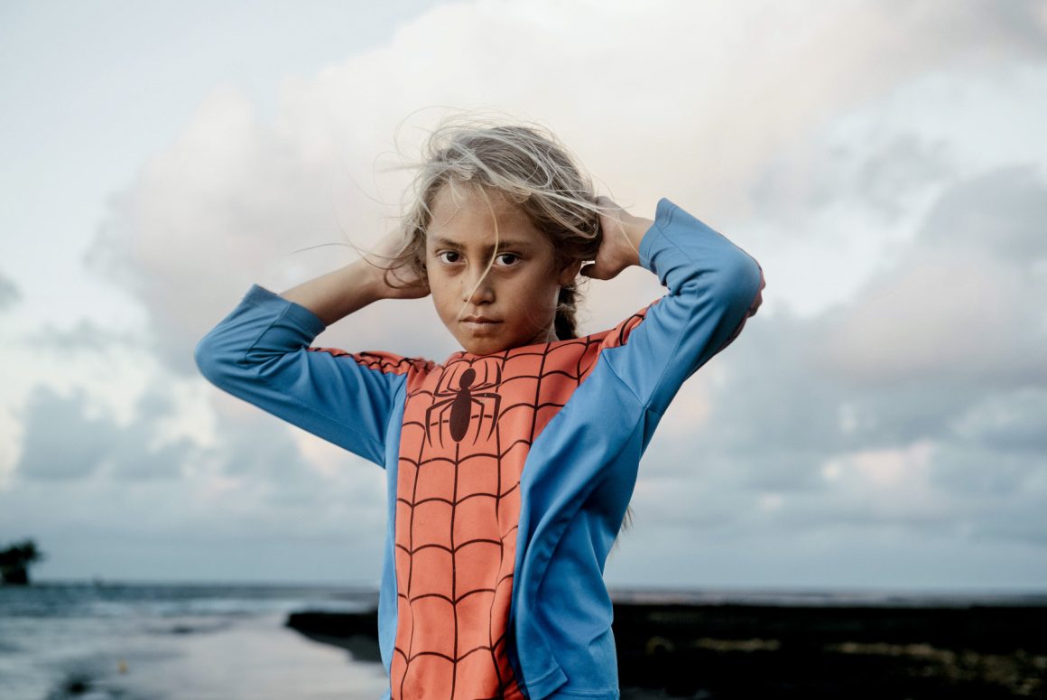 A young girl in a Spider-Man top stands beside the ocean in French Polynesia. Photo by Hélène Havard.