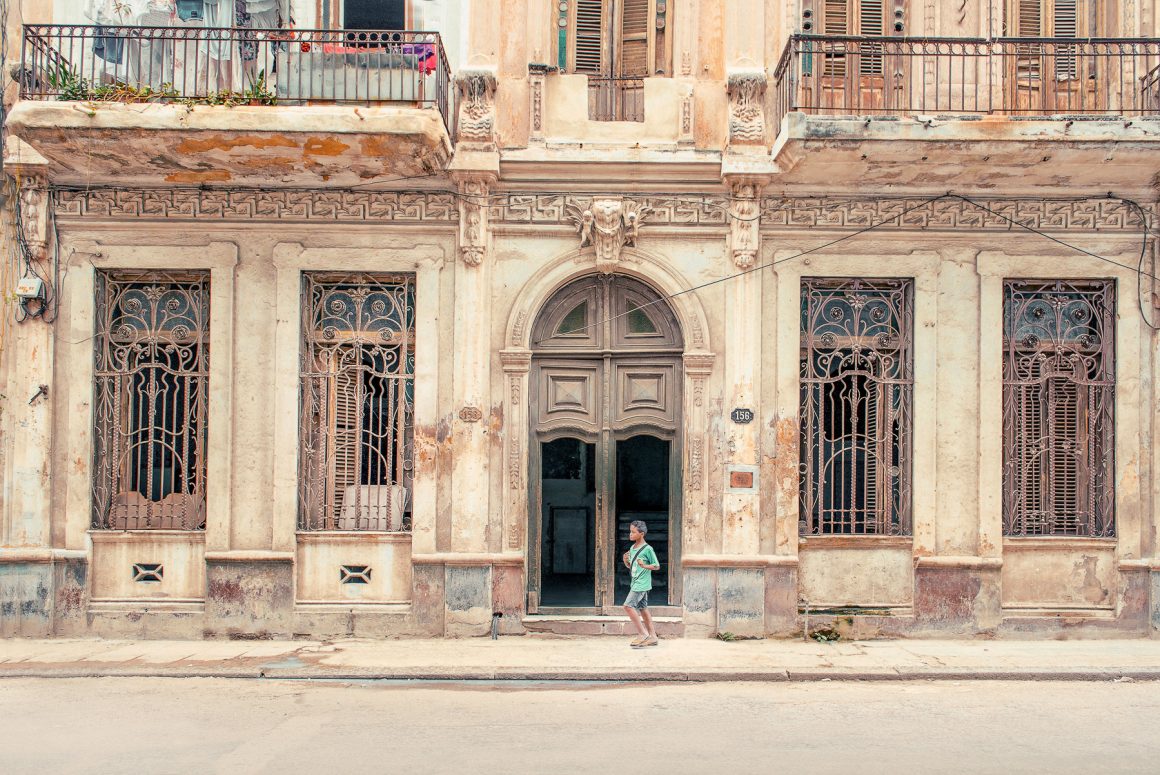 A child walks past an ornate, weathered historic house in Havana, Cuba. Photo by Hélène Havard.