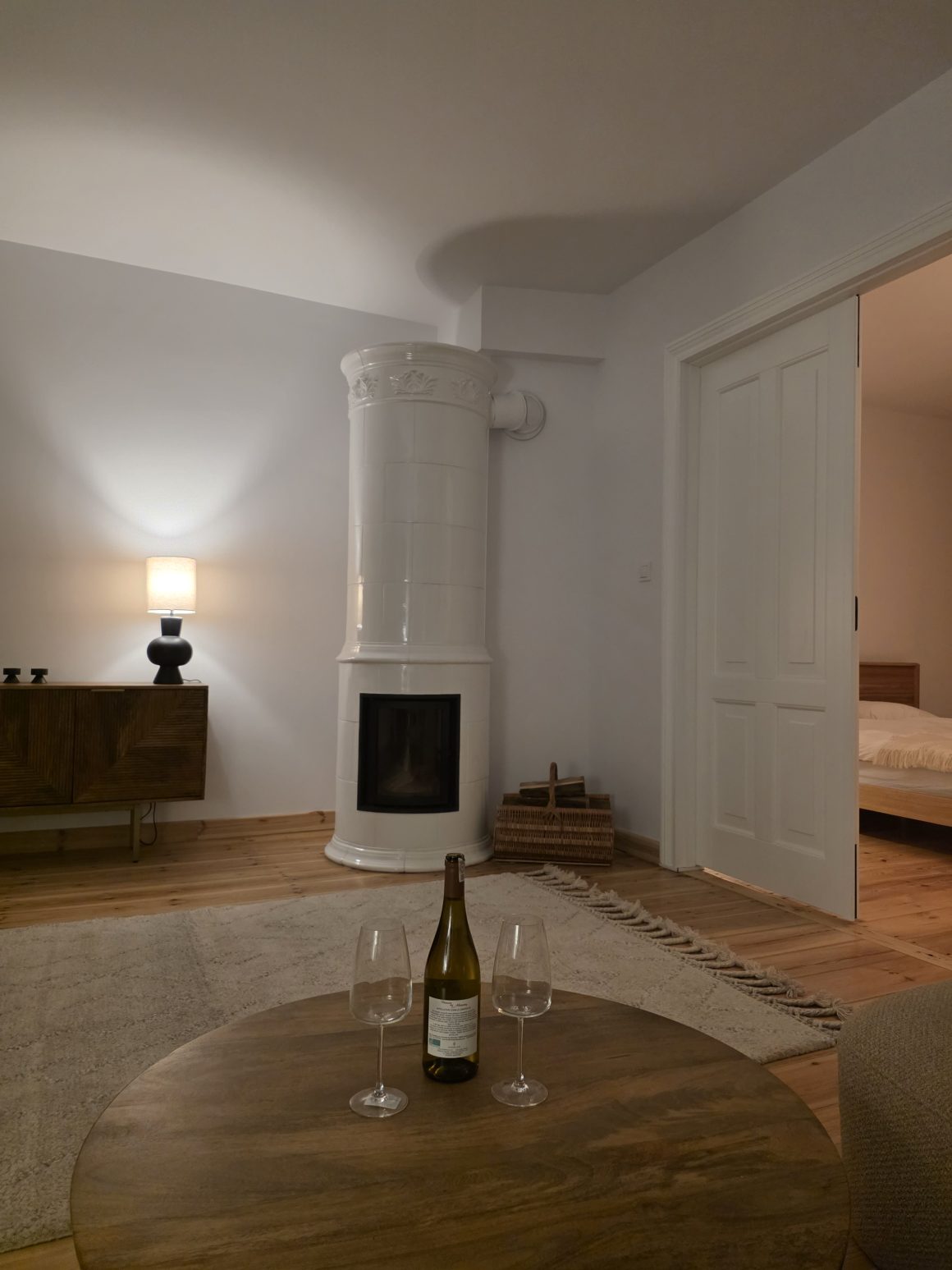 Cozy living room with a white tiled fireplace, wine bottle, and two glasses.
