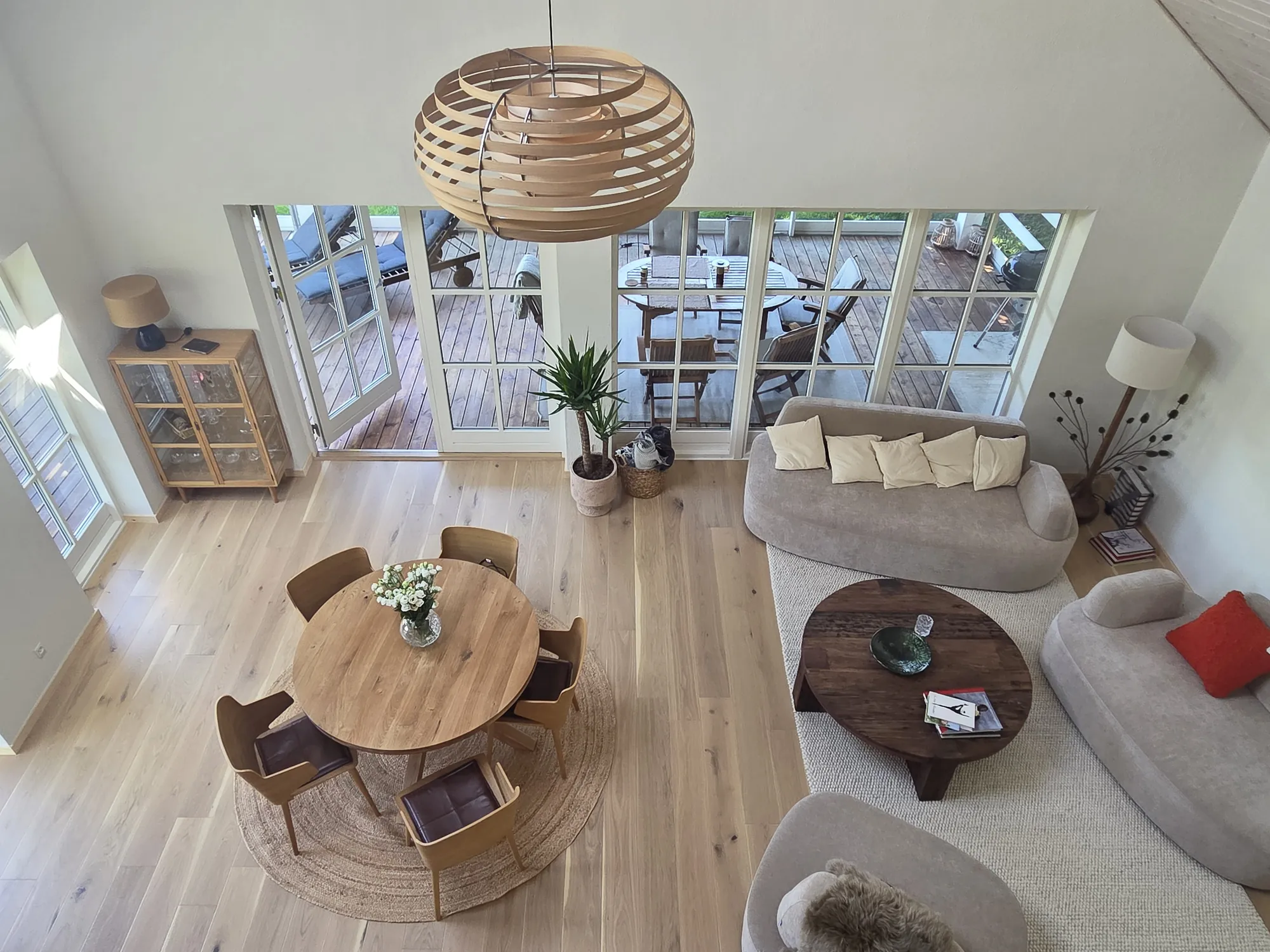 Scandinavian living room seen from above, with a bent-wood pendant lamp, round oak dining table and curved sofas