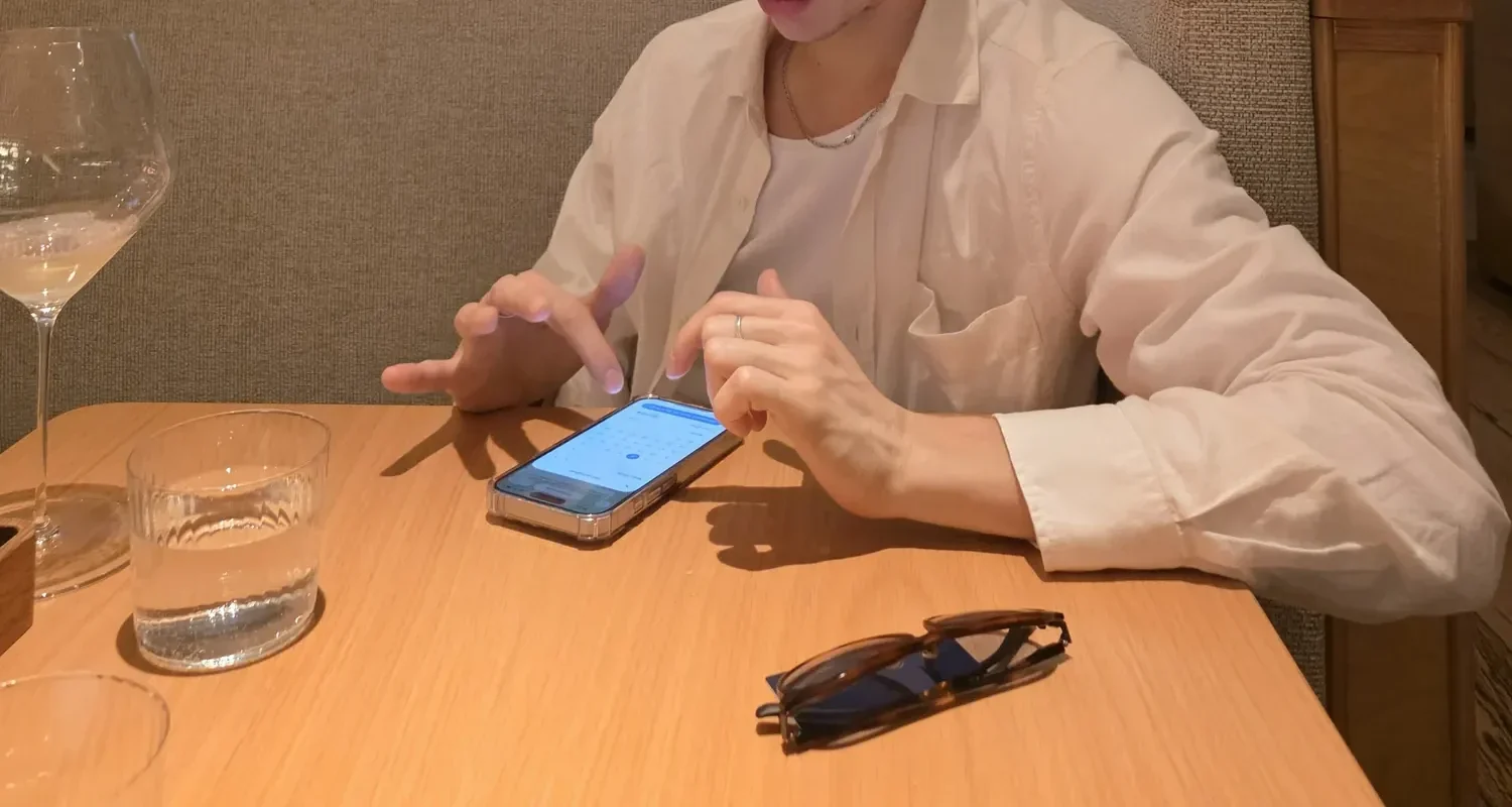 Traveler in a white linen shirt checking dates on a phone at a restaurant table in the evening