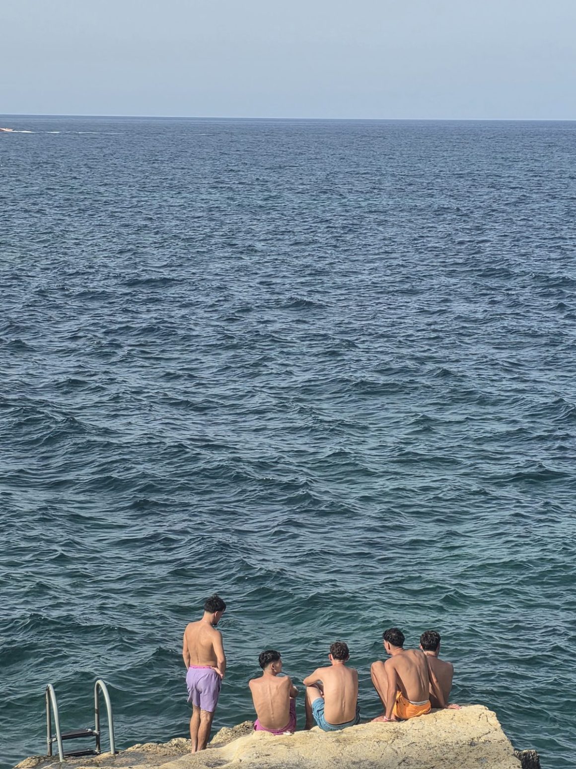 Five young travelers sitting on the rocks at a Swimming spot, looking out over the Mediterranean