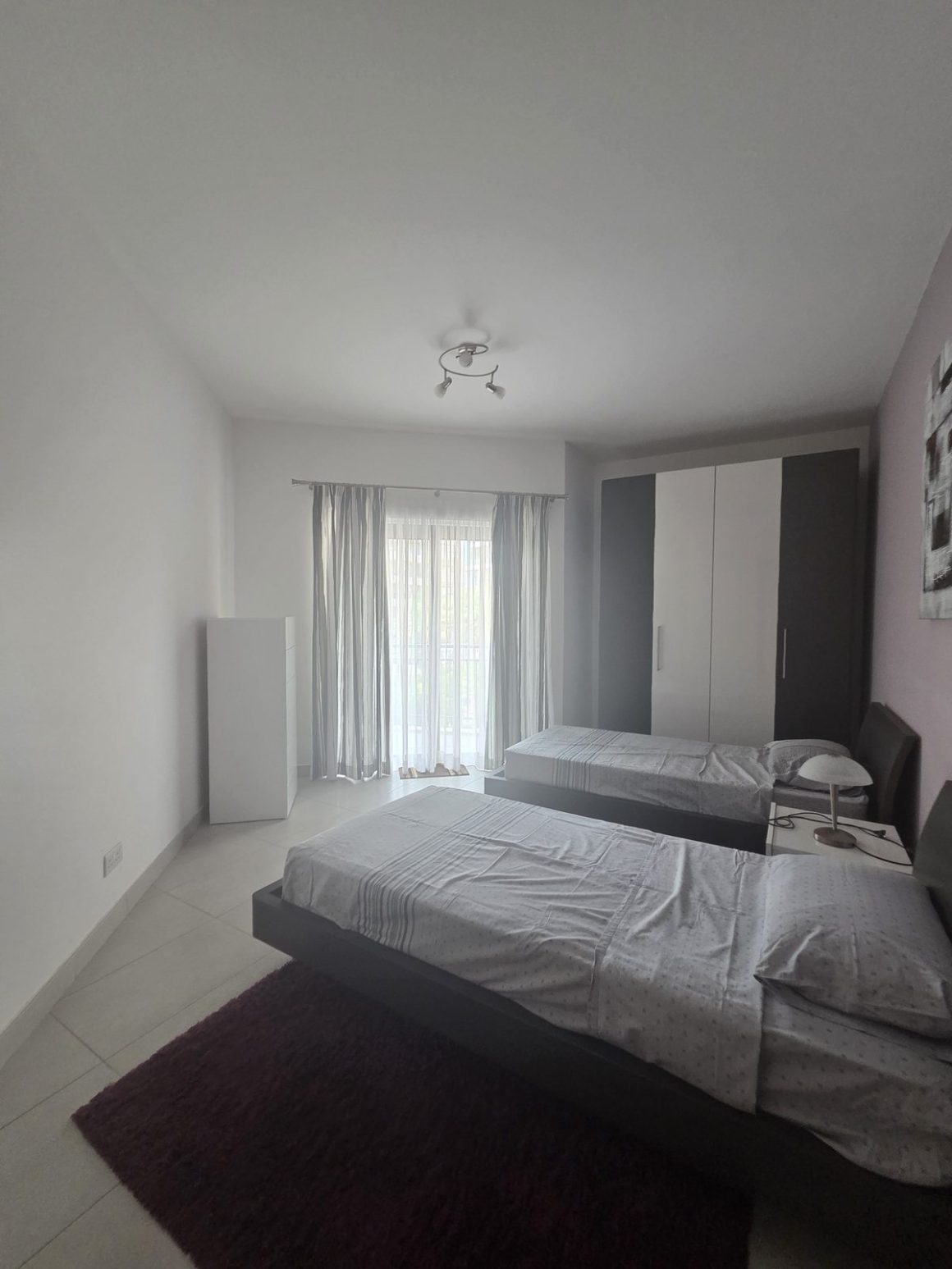 A twin bedroom in a Maltese holiday apartment, with two single beds, wardrobe and balcony door