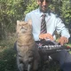 Fery Lionfarsi plays a MIDI keyboard in a blue shirt and striped tie as his tabby cat sits beside him with its eyes closed