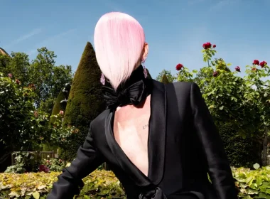 Fredrik Robertsson in a nude masked look and platform shoes, posing against a green wall with dried flowers