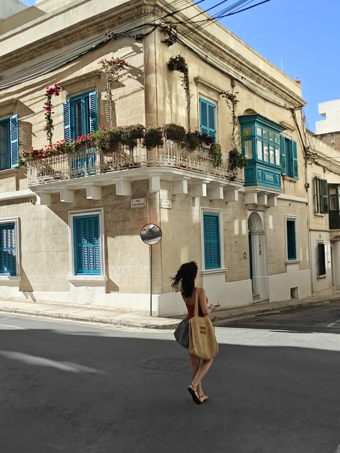 Woman walking past a limestone townhouse with blue shutters and a traditional Maltese balcony in Sliema